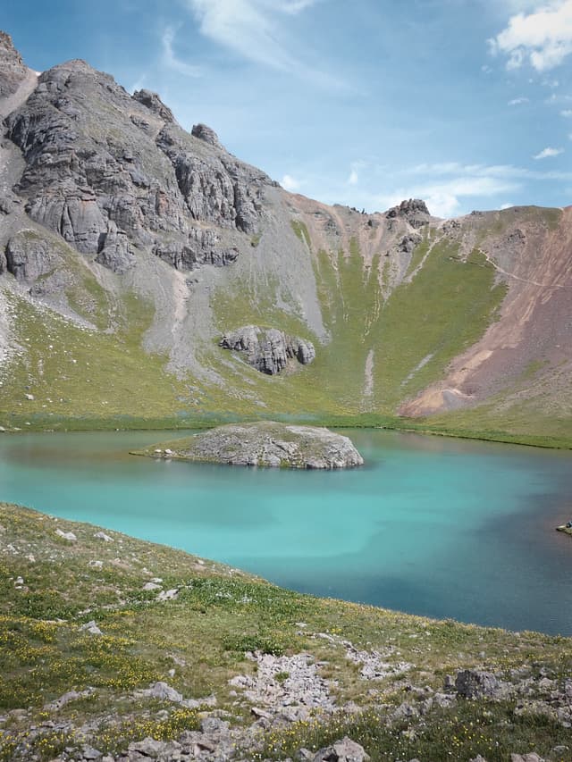 Turquoise alpine lake surrounded by steep rocky mountains and green grassy slopes under a partly cloudy blue sky